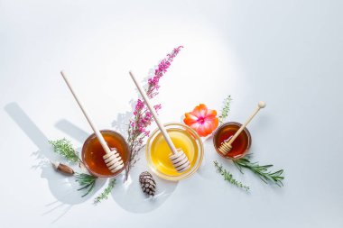 Beyaz zemin üzerinde bal çubukları ve çiçeklerle bal kavanozlarının kompozisyonu.