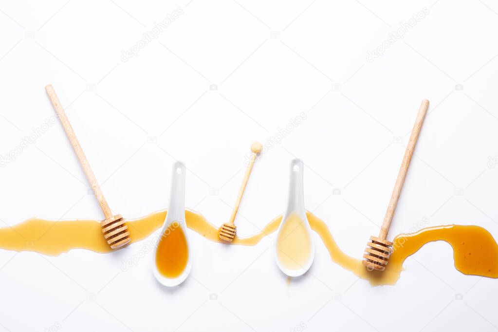 white spoons and honey sticks, with spilled honey,  isolated on white background.