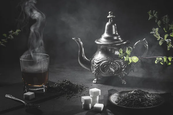 ミントの蒸しカップと伝統的なモロッコのティーポットは スモーキーな黒い雰囲気の中で モロッコ茶のコンセプト — ストック写真