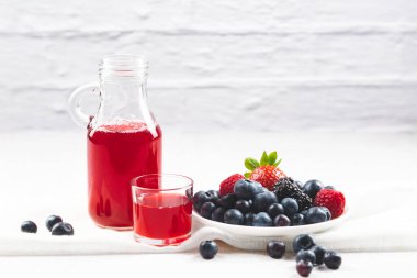 Beyaz tabakta böğürtlenler ve sürahide detoks suyu ve beyaz arka planda cam..