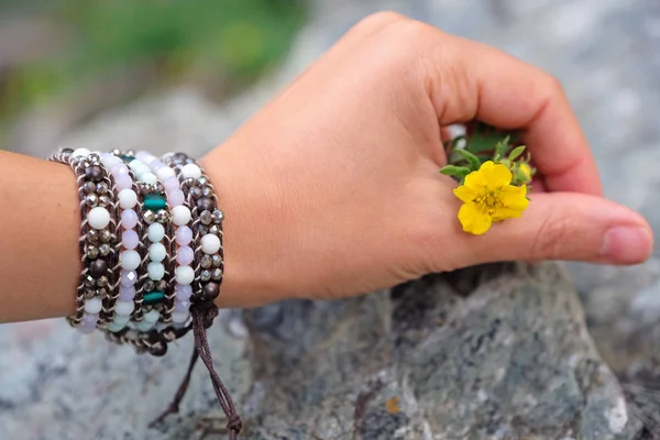 Női kéz fogja a sárga virágot a sziklák között. — Stock Fotó