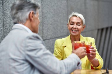 - Şerefe. Sarı takım elbiseli neşeli ve güzel orta yaşlı bir kadın arkadaşıyla kokteyl içiyor ve dışarıda kafede birlikte otururken gülümsüyor.
