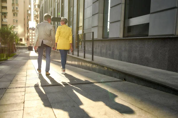 정장을 입고 손을 잡고 함께 시내 거리를 걷고 있는 세련 된 중년 부부의 모습 — 스톡 사진