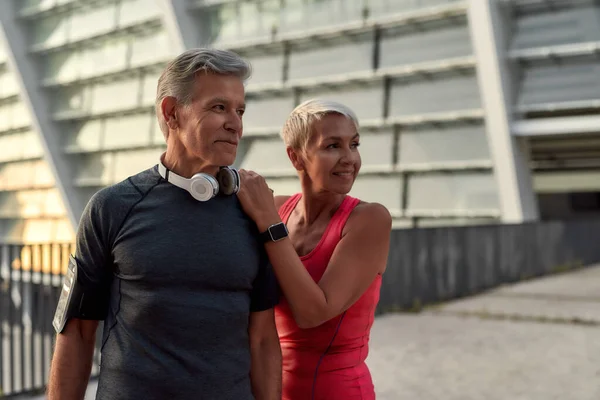 Kochamy sport. Portret szczęśliwej pary w średnim wieku w sportowej odzieży odwracającej wzrok z uśmiechem podczas treningu na świeżym powietrzu — Zdjęcie stockowe