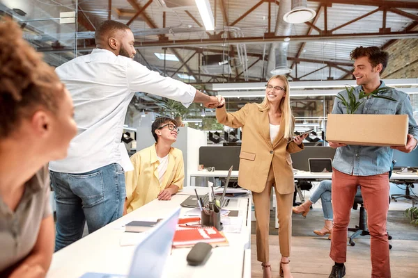 Nice to meet you. Young beautiful woman in suit giving fist bump to her new coworker while standing in the modern office with other colleagues — Stock Photo, Image