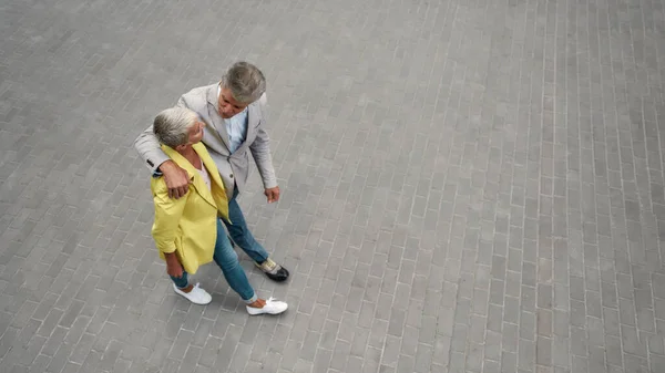 Проводим время вместе. Вид сверху на стильную зрелую пару, обнимающуюся и гуляющую вместе по городской улице — стоковое фото