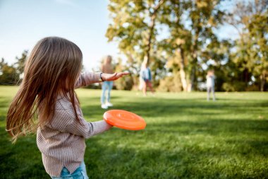 Making memories, breaking the distance. Little girl playing frisbee with her family in the park on a sunny day clipart
