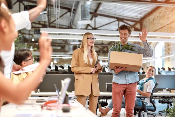 ¿Hola? Joven hombre guapo en ropa casual saludando a sus nuevos compañeros de trabajo y sonriendo mientras está de pie en la oficina moderna — Foto de Stock