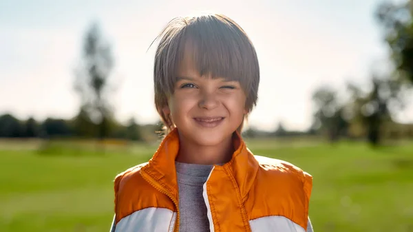 Spaß haben. Porträt eines niedlichen lächelnden Jungen, der an einem sonnigen Tag mitten im Park in die Kamera blickt — Stockfoto