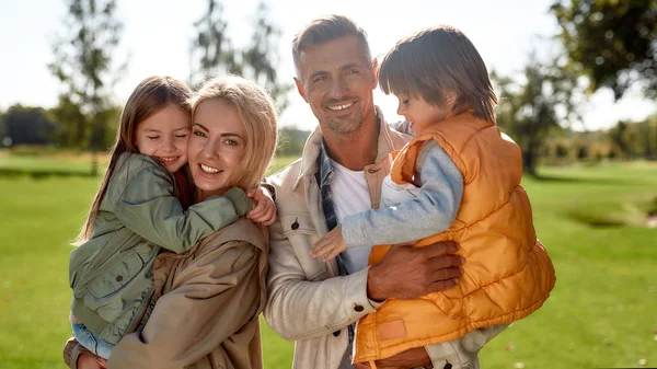 Hija e hijo. Retrato de familia feliz y hermosa con niños mirando a la cámara con sonrisa mientras están de pie en el parque en un día soleado —  Fotos de Stock