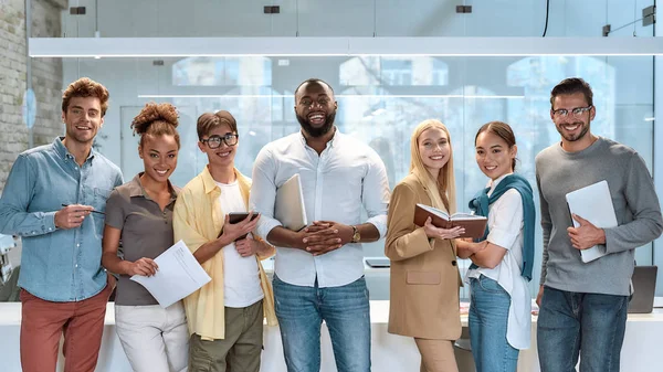 Drömarbete. Porträtt av unga och framgångsrika medarbetare i vardagskläder som ler mot kameran när de står i arbetsrummet — Stockfoto