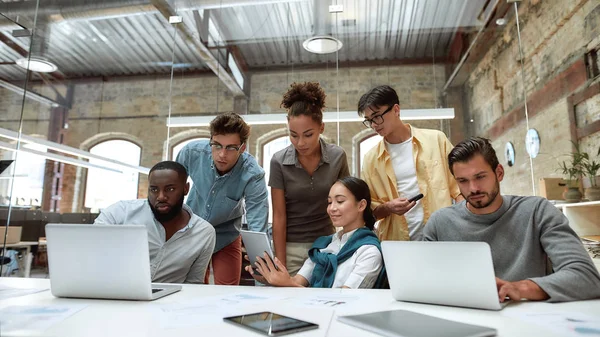 Successful multicultural team. Young business people in casual wear using modern technologies and working together on new project while sitting in the creative office — Stock Photo, Image