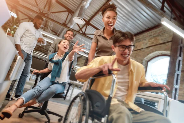 Being disabled does not mean you cant be happy. Young positive asian man in wheelchair having fun with his colleagues at modern office — ストック写真