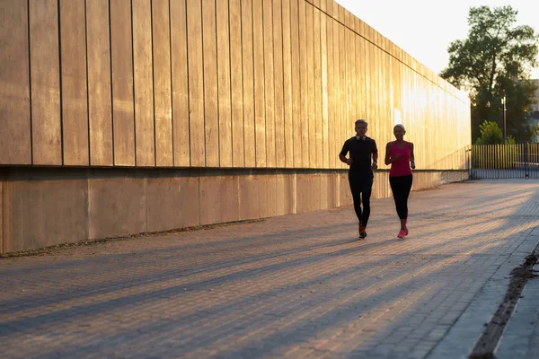 Vi tränar alltid tillsammans. Senior par i sportkläder som löper tillsammans genom stadens gata på morgonen — Stockfoto