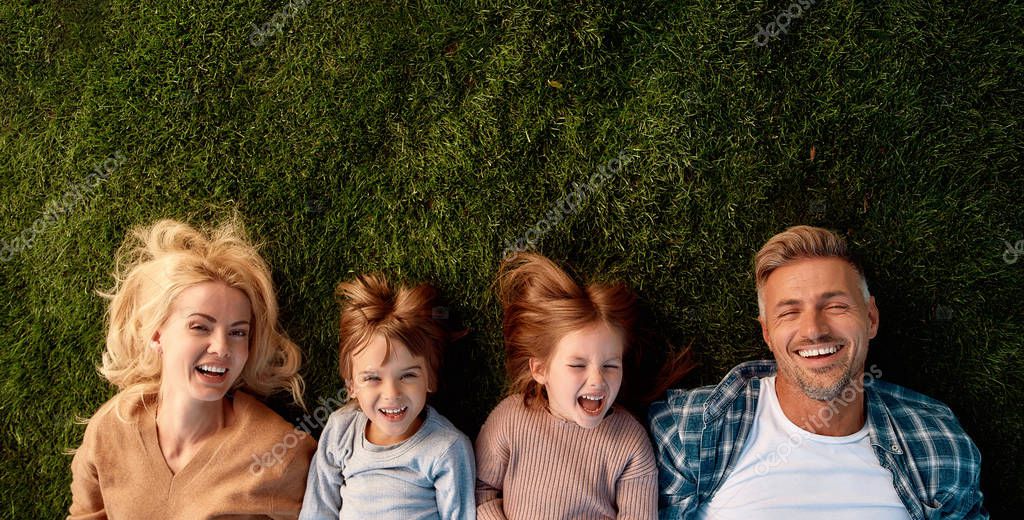 Top view of smiling parents, little girl and boy having fun while lying on a grass. Children, family and nature concept. Horizontal shot