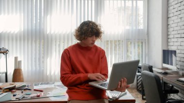 Sanat yönetmeni. Modern ofiste dikilirken dizüstü bilgisayarla çalışan sıradan giysili bir adam. Yaratıcı insanlar