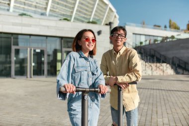 İyi hafta sonları. Güneşli bir günde iki arkadaş elektrikli scooter sürerken eğleniyor.