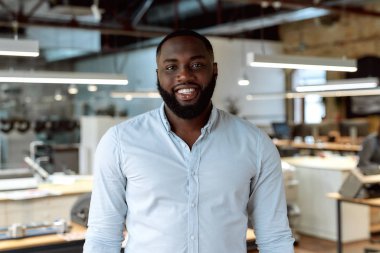 Mutlu bir çalışan sağlıklı bir ofis yapar. Ofiste poz veren kendinden emin bir erkek işçi.