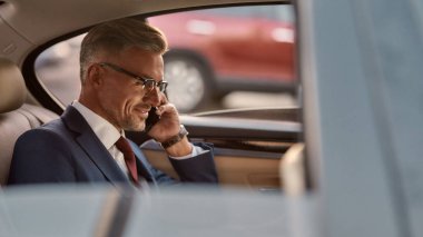 Her zaman müsaidim. Klasik giyinmiş neşeli, olgun bir adamın yan görünüşü arabada oturup müşteriyle telefonda konuşması.