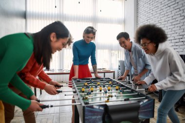 Mutlu takım. Bir grup genç ve çok kültürlü insan modern ofiste masa futbolu oynayıp gülüyorlar. Ofis aktiviteleri. Birlikte eğleniyoruz. Mutlu çalışanlar