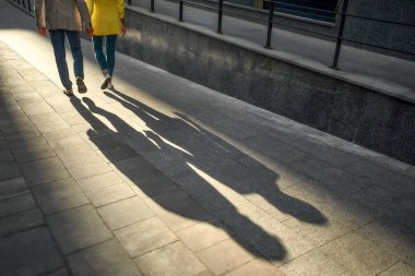 Sıradan giysiler içinde el ele tutuşan ve şehir caddesinde birlikte yürüyen bir çiftin kesilmiş fotoğrafı.