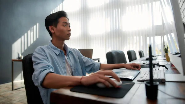 Designer at work. Serious young asian man in casual wear working with computer while sitting at his workplace in the modern office. Creative agency — Stock Photo, Image