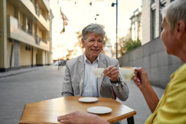 A divertirmo-nos juntos. Casal sênior feliz e elegante desfrutando de café enquanto sentado no café ao ar livre — Fotografia de Stock