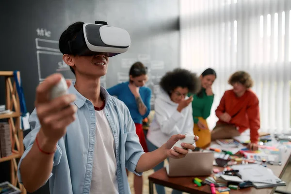 La evolución de VR Technologies. Joven hombre asiático en ropa casual vistiendo casco de realidad virtual y sonriendo mientras sus colegas discuten nuevo proyecto detrás de él. Alta tecnología —  Fotos de Stock