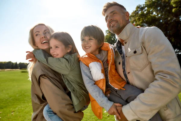 Des moments heureux. Les jeunes parents et leurs enfants s'amusent ensemble et sourient en se tenant debout sur une prairie verte — Photo