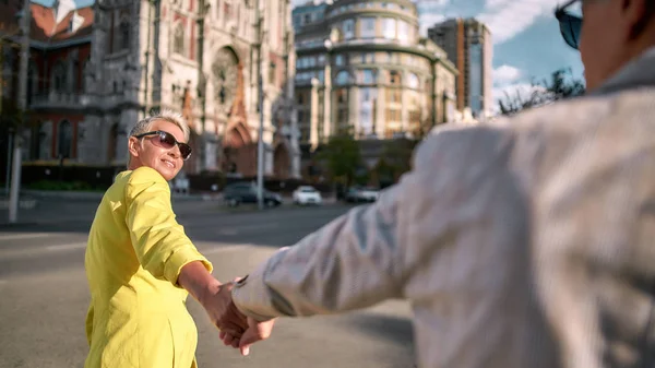 Mooie en gelukkige vrouw van middelbare leeftijd die man bij de hand houdt en glimlacht terwijl ze samen otdoors loopt — Stockfoto