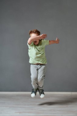 Deliriyorum. Stüdyoda zıplayan ve el kol hareketi yapan sıradan kıyafetlerle heyecanlı küçük bir çocuğun tam boy portresi. Çocukluk. Hareket