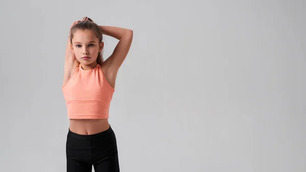 Mais apto, mais saudável, mais feliz. Flexível bonito menina criança olhando para a câmera ao esticar seu corpo isolado em um fundo cinza. Esporte, fitness, conceito de estilo de vida ativo. Tiro horizontal . — Fotografia de Stock