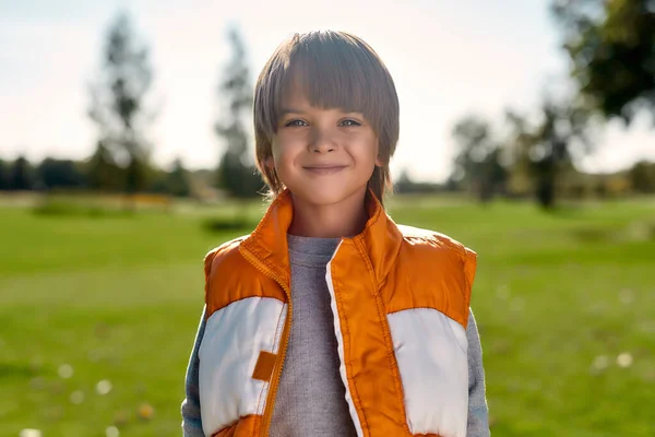 Ευτυχισμένο παιδί. Πορτρέτο ενός χαριτωμένου χαμογελαστού αγοριού στέκεται στη μέση του πάρκου σε μια ηλιόλουστη μέρα — Φωτογραφία Αρχείου