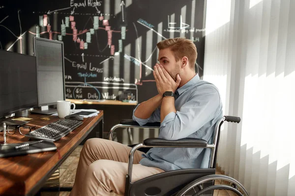 No puede ser verdad. Retrato de un joven comerciante sorprendido en una silla de ruedas mirando gráficos en las pantallas de la computadora y sintiéndose molesto mientras trabajaba en su lugar de trabajo en la oficina —  Fotos de Stock