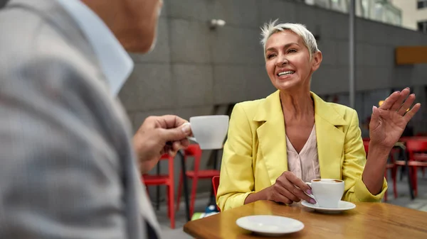 A descansar num café. Feliz casal maduro desfrutando de café e sorrindo enquanto sentado no terraço do café — Fotografia de Stock