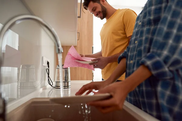 Perfeitamente limpo. Casal feliz em roupas casuais lavar os pratos juntos, enquanto em pé em sua cozinha moderna — Fotografia de Stock