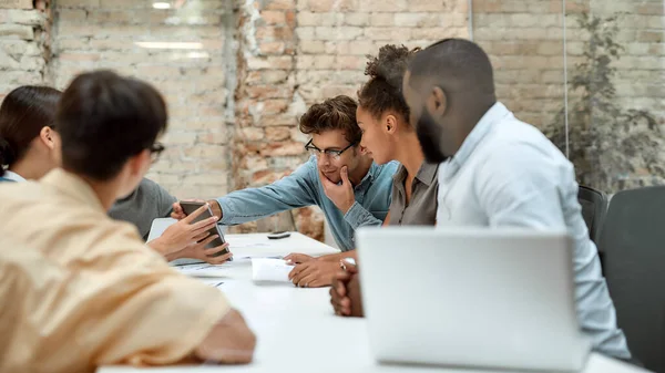 Professionisti. Giovane bell'uomo che guarda tablet digitale mentre lavora con i colleghi nel moderno ufficio — Foto Stock