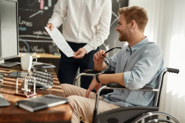 良い結果を達成する。オフィスで働く同僚と財務報告を話し合い笑顔で話す車椅子の若い幸せなビジネスマン. — ストック写真
