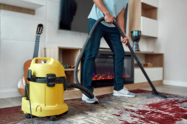 Ausgeschnittene Ansicht eines jungen Mannes, der während seiner Arbeit im modernen Wohnzimmer den Teppich mit Staubsauger reinigt. Professionelle Reinigungskraft bei der Arbeit — Stockfoto