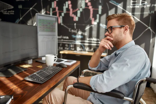 Aku harus berpikir. Pandangan sampingan pedagang laki-laki muda yang terfokus di kursi roda memikirkan sesuatu ketika bekerja di tempat kerjanya di kantor modern — Stok Foto