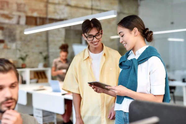 We did it. Two asian colleagues in casual wear looking at digital tablet and discussing something while standing in the creative office — Stock Photo, Image