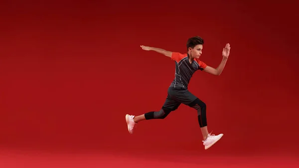 Κουνήσου. Ένα έφηβο αγόρι ασχολείται με τον αθλητισμό, κοιτάζει αλλού ενώ πηδάει. Απομονωμένο σε κόκκινο φόντο. Γυμναστική, εκπαίδευση, ενεργός τρόπος ζωής. Οριζόντια βολή — Φωτογραφία Αρχείου