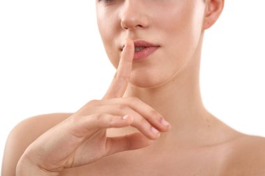 Sırrımı sakla. Güzel, şehvetli bir kadın, beyaz arka planda dururken parmağını dudaklarından ayırmıyor.