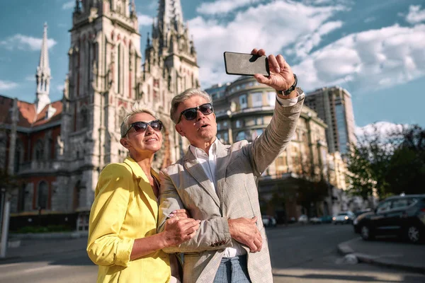 Ερωτευτείτε. Ευτυχισμένο και χαρούμενο ώριμο καυκάσιο ζευγάρι με γυαλιά ηλίου να βγάζει selfie από κινητό τηλέφωνο και να χαμογελά ενώ περνάει χρόνο μαζί σε εξωτερικούς χώρους — Φωτογραφία Αρχείου