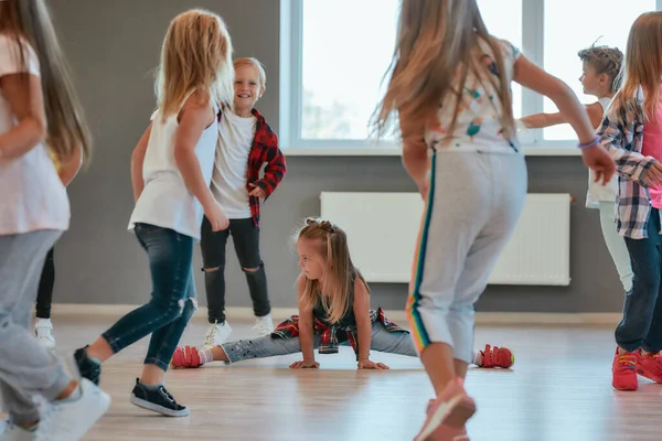 Gymnastic exercises. Little cute girl sitting on a twine while having a choreography class. Group of positive and active children learning a modern dance in the dance school — 스톡 사진