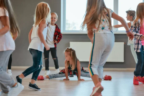 Ejercicios gimnásticos. Niña linda sentada en un cordel mientras tiene una clase de coreografía. Grupo de niños positivos y activos aprendiendo un baile moderno en la escuela de baile —  Fotos de Stock