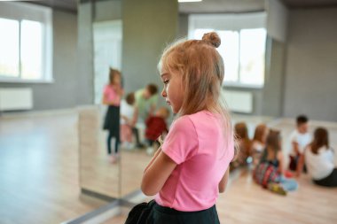 Thinking about something. Back view of a little cute girl looking away and dreaming while standing in the dance studio. Group of children having a choreography class. Activity. Dance school