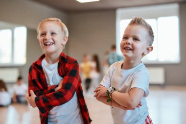 Cool dancers. Two fashionable boys in casual clothes keeping arms crossed and smiling while standing in the dance studio