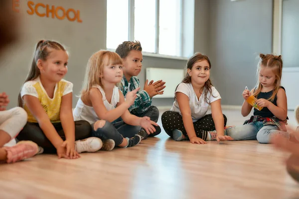 Eine Pause einlegen. Eine Gruppe kleiner süßer Mädchen und Jungen, die auf dem Boden sitzen und im Tanzstudio miteinander reden. Choreographiekurs — Stockfoto