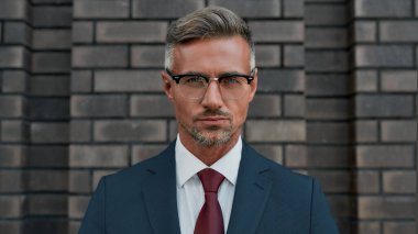 Gözlüklü yakışıklı işadamının portresi dışarıda duvara yaslanmış kameraya bakıyor.